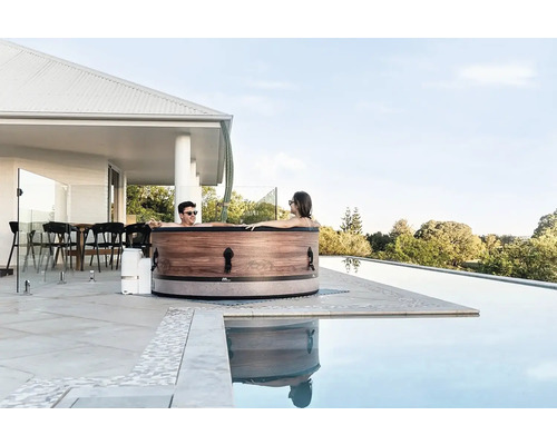 Cuplu relaxându-se într-o cadă cu hidromasaj pe o terasă lângă o piscină.