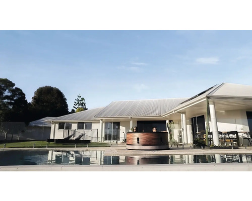 Vedere de sus a unei căzi fierbinți din lemn, lângă o piscină, în fața unei case de locuit.