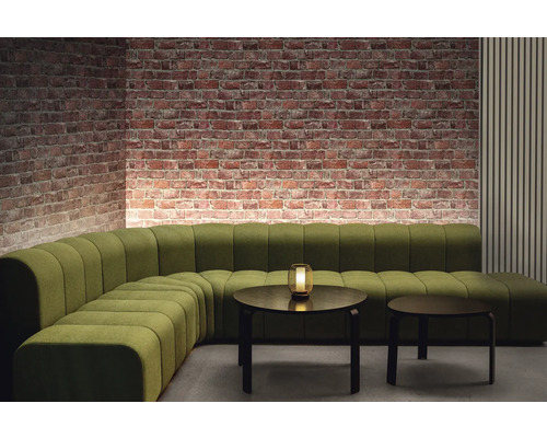 Vedere a camerei cu canapea modulară verde, două mese rotunde și perete din cărămidă