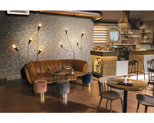 Interiorul unei cafenele cu canapea, mese, scaune și aplice de perete în fața unui perete de cărămidă