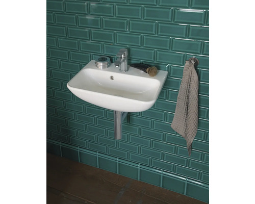 Chiuvetă de baie cu robinet și prosop în fața unui perete cu gresie