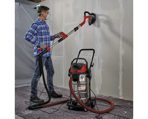 Un bărbat folosește o șlefuitoare pentru gips-carton cu aspirator pe un perete.