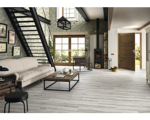 Cameră de zi luminoasă cu scară de piatră, canapea, masă din lemn, sobă și gresie cu aspect de lemn.