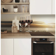 Scenă de bucătărie cu un panou de protecție împotriva stropilor, două pahare de vin și ustensile de bucătărie pe un blat de lucru