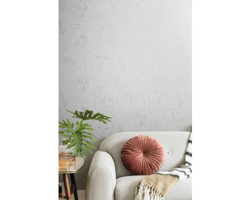 Cameră de zi cu tapet cu chipuri de femei, canapea, pernă, plantă și masă