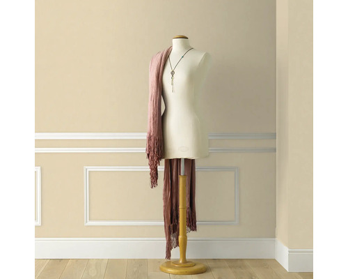 Mannequin de croitorie cu eșarfă și colier în fața unui perete cu muluri decorative