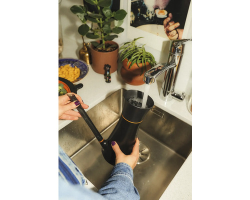 O persoană umple un ceainic negru cu apă într-o chiuvetă de bucătărie.