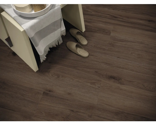 Fotografie de interior a unei camere cu podea laminată cu aspect de lemn, un taburet mic și papuci de casă.