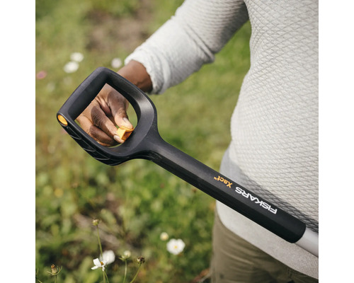 Prim-plan cu o persoană care ține o cazma Fiskars pentru a lucra în grădină.