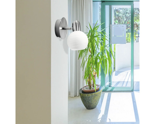 Lămpă de perete cu abajur rotund, striat, lângă o plantă de interior într-o cameră luminoasă.