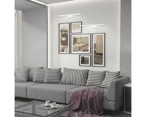 Cameră de zi cu canapea gri, perne cu model în dungi, tablouri pe perete și două lămpi de perete