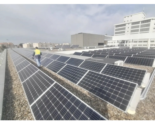 Fotografie cu panouri solare pe un acoperiș cu o persoană care poartă o vestă de siguranță