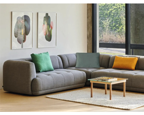 Cameră de zi cu canapea de colț gri, perne, măsuță de cafea și picturi murale