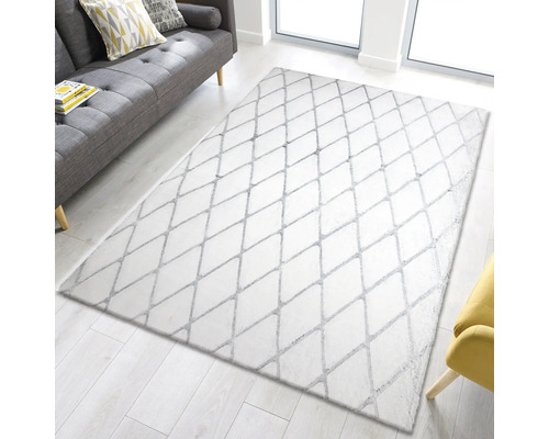 Covor alb cu model de romburi pe podea de lemn deschisă, canapea și fotoliu în fundal.