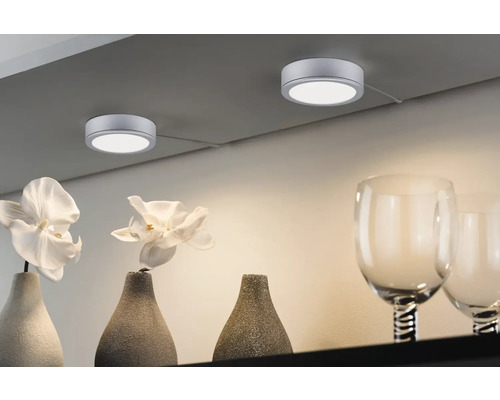 Două spoturi rotunde cu LED montate pe tavan iluminează vaze și pahare pe un raft.