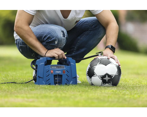 Un bărbat umflă o minge de fotbal cu un compresor pe un gazon.