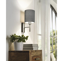Lampa de perete cu abajur din material textil deasupra comodei din lemn cu plantă la ghiveci