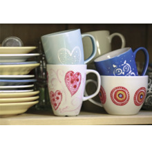 Stivă de căni ceramice cu diverse decorațiuni și farfurii pe raft.