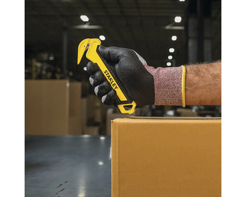 Mână cu mănușă ținând un tăietor de cuțite Stanley deasupra unei cutii de carton
