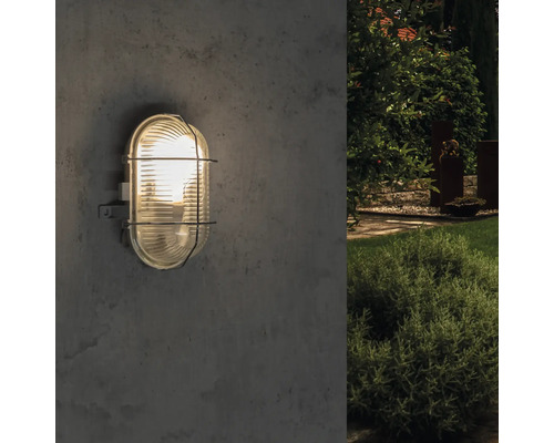 Lumină de exterior ovală cu grilaj de protecție montată pe un perete.