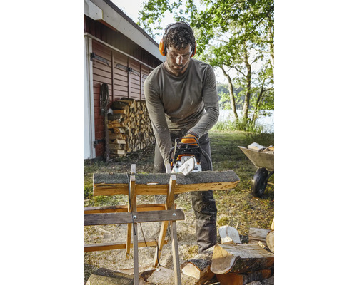 Bărbat taie lemne cu un ferăstrău cu lanț pe un capră de lemn afară