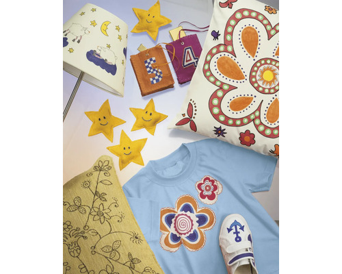 Scenă decorativă cu o abajur, perne, un tricou, stele și pandantive, care emană o atmosferă confortabilă și creativă.