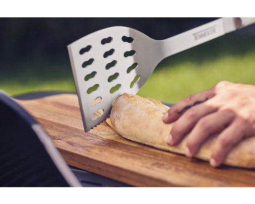 Spatulă grătar din oțel inoxidabil care taie pâine pe un tocător din lemn.
