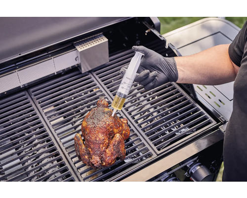 O persoană injectează cu o seringă lichid într-un pui la grătar pe un grătar.