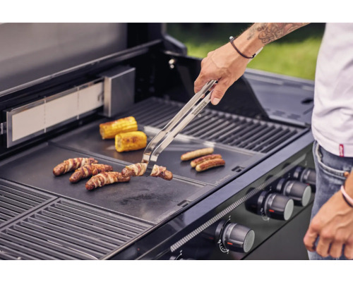 O persoană face la grătar cârnați, șuncă și porumb pe grătar.