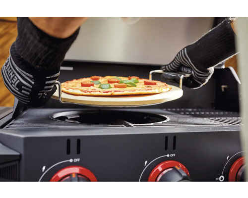 Pizza pe o piatră de pizza este împinsă într-un grătar pe gaz