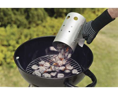 Persoană turnând cărbune dintr-un coș de aprindere într-un grătar sferic.