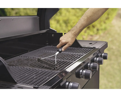 O persoană curăță un grătar cu o perie de grătar.