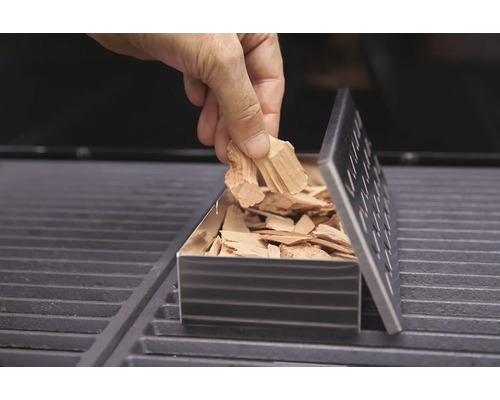 Umplerea unei cutii de afumare cu așchii de afumare pe un grătar