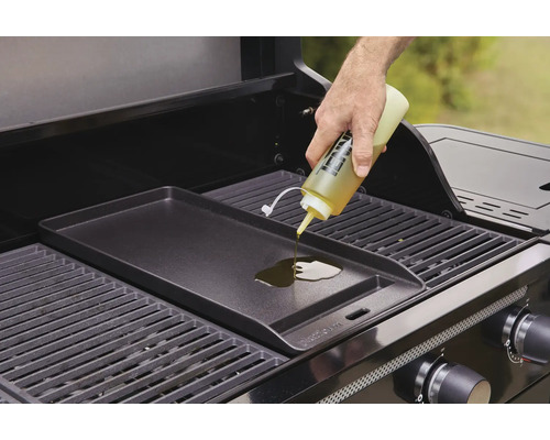 O persoană toarnă ulei pe o plită pe un grătar pe gaz.
