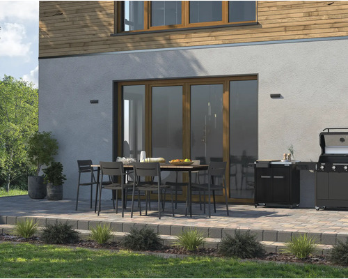 Spațiu exterior cu masă de grădină, scaune și grătar pe o terasă lângă o casă.