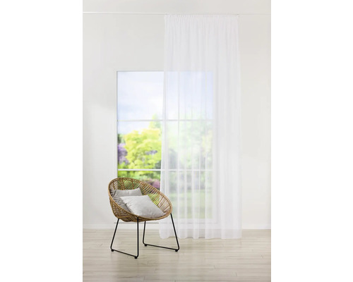 Cameră luminoasă cu fotoliu din ratan, perne și o perdea transparentă în fața unei ferestre