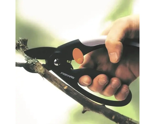 O mână taie o ramură cu o foarfecă de grădină Fiskars.