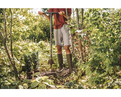 O persoană folosește o unealtă de făcut gropi pentru plantare în grădină pentru a planta un copac mic.