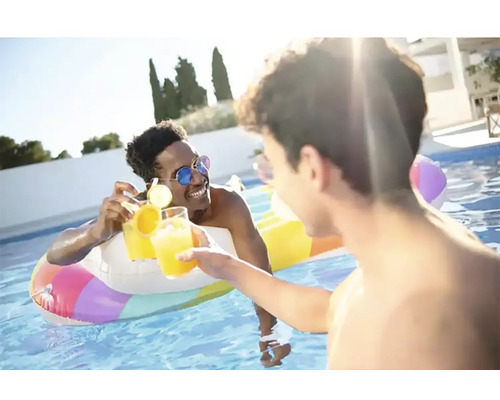 Doi bărbați ciocnesc pahare cu băuturi într-o piscină cu un colac gonflabil.