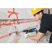 Un bărbat găurește un perete cu un ciocan rotopercutor. Poartă echipament de protecție.