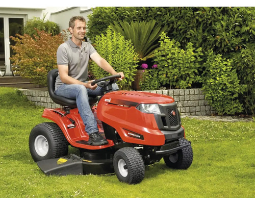 Un bărbat conduce un tractor de tuns iarba roșu pe un gazon.