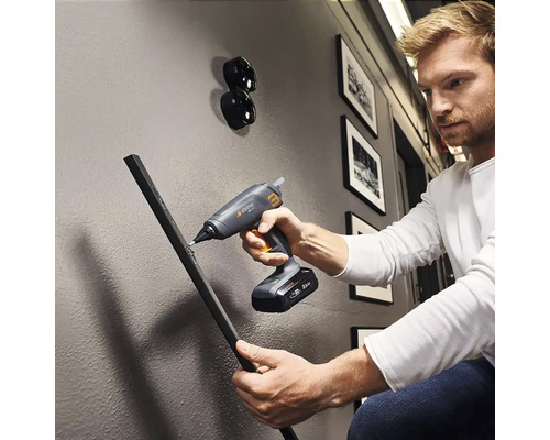 Un bărbat folosește un pistol de lipit cu acumulator pentru a fixa o piesă de lucru pe un perete.