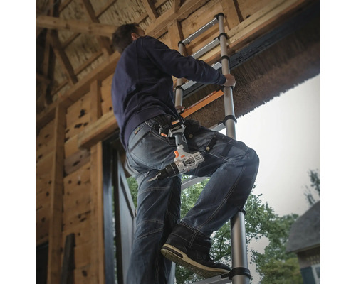 Muncitor pe o scară telescopică cu o șurubelniță fără fir la curea la lucru.