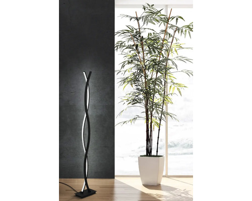 Lampă de podea modernă cu design curbat și iluminare LED lângă o plantă de interior într-o cameră luminoasă.