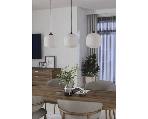 Trei lămpi suspendate albe cu abajururi din sticlă canelată deasupra unei mese din lemn într-o sufragerie