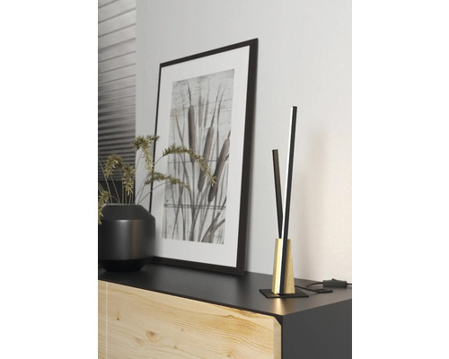 Aranjament decorativ cu lampă de masă, imagine înrămată și plantă pe o comodă.