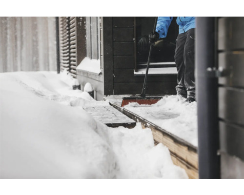 Persoană care îndepărtează zăpada cu o lopată de zăpadă în fața unei case.