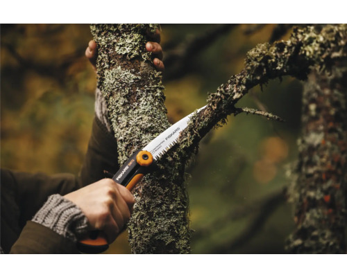 O persoană taie o ramură cu un ferăstrău Fiskars.