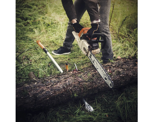 O persoană taie un trunchi de copac cu un lanț, cu un fierăstrău de ramuri în iarbă.