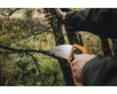 Prim-plan cu o persoană care taie o ramură cu un fierăstrău manual Fiskars.
